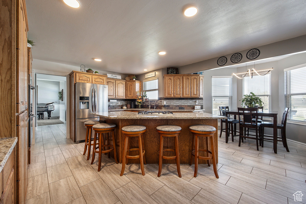 Kitchen featuring stainless steel fridge, wood finish floors, backsplash, a kitchen bar, and recessed lighting
