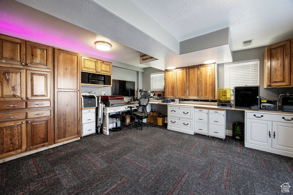Office space featuring dark carpet, built in study area, a textured ceiling, and healthy amount of natural light