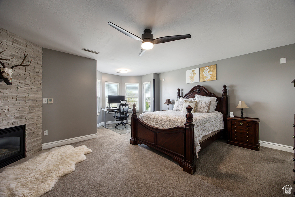 Carpeted bedroom featuring an office area, a ceiling fan, and a stone fireplace