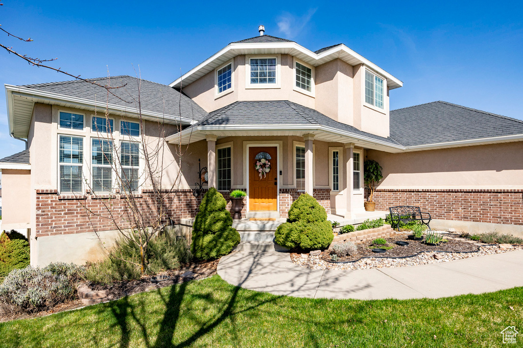 View of front of home with stucco siding, brick siding, covered porch, and a shingled roof
