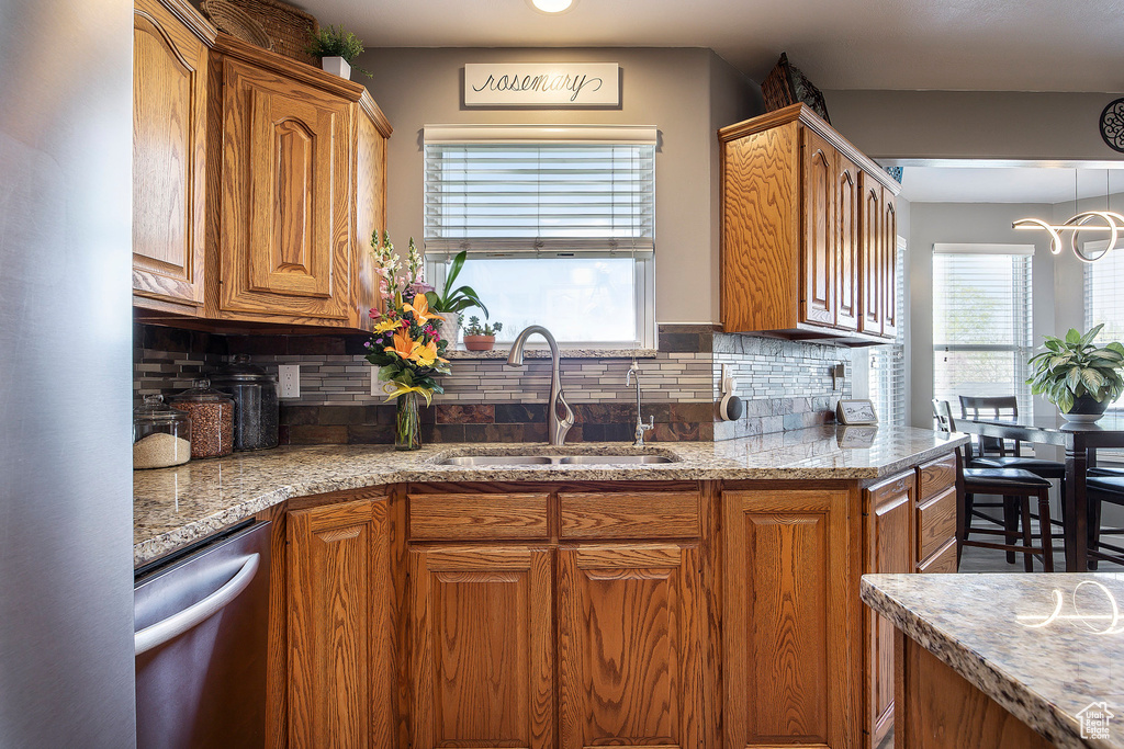 Kitchen with stainless steel appliances, brown cabinets, decorative backsplash, and light stone countertops