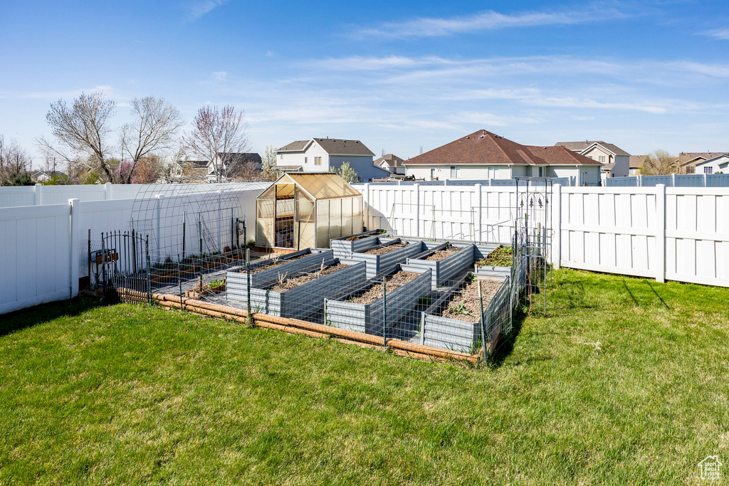 Fenced backyard with a garden, a greenhouse, a residential view, and an outbuilding