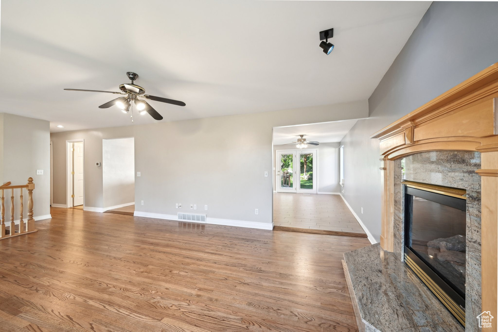 Unfurnished living room featuring a ceiling fan, wood finished floors, a premium fireplace, and baseboards