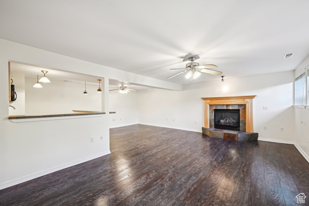 Unfurnished living room with a ceiling fan, a tile fireplace, wood finished floors, and baseboards