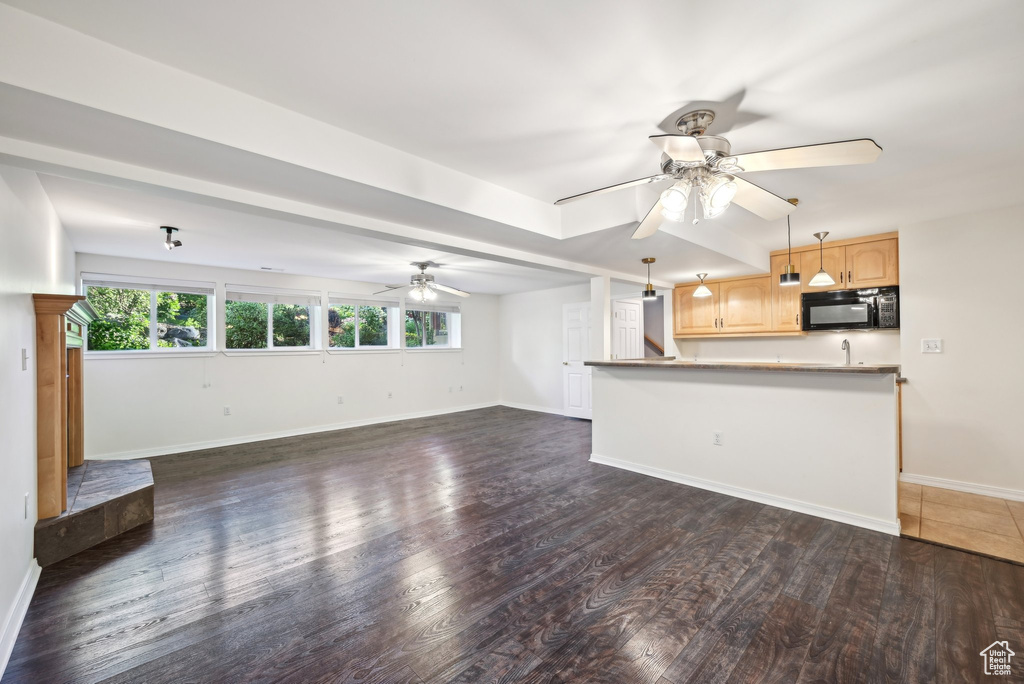 Unfurnished living room featuring a ceiling fan, dark wood-style floors, and baseboards