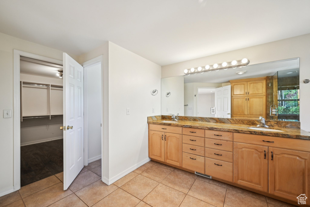 Full bathroom with double vanity, a walk in closet, tile patterned floors, an enclosed shower, and baseboards