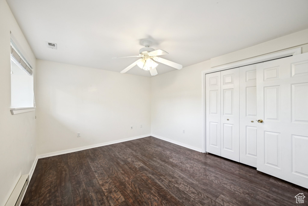 Unfurnished bedroom featuring baseboard heating, dark wood finished floors, a closet, baseboards, and ceiling fan