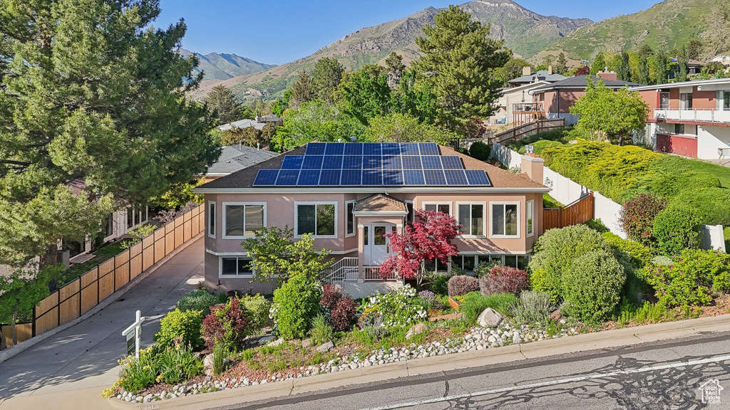 View of front of property with roof mounted solar panels, a mountain view, stucco siding, and a chimney