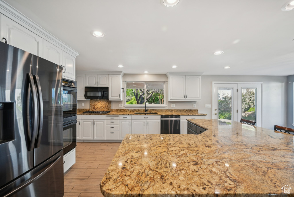 Kitchen with black appliances, a sink, light wood-type flooring, white cabinetry, and light stone countertops