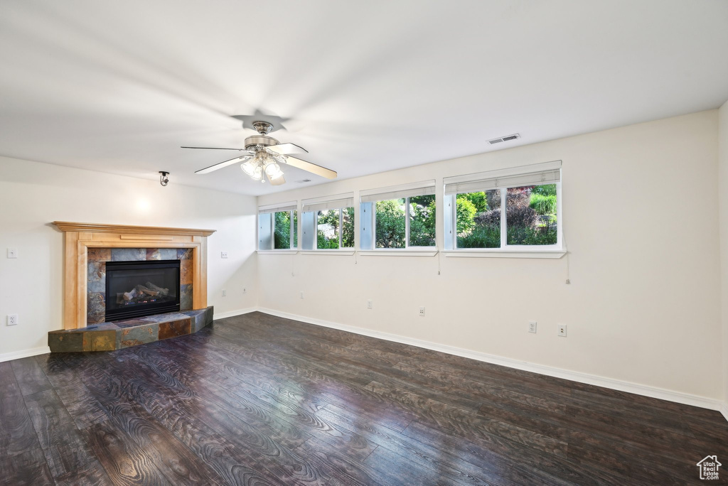 Unfurnished living room featuring wood finished floors, a tile fireplace, baseboards, and a ceiling fan