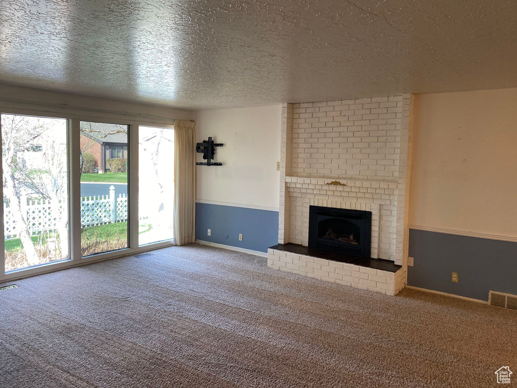 Unfurnished living room with a textured ceiling, a brick fireplace, carpet, and visible vents