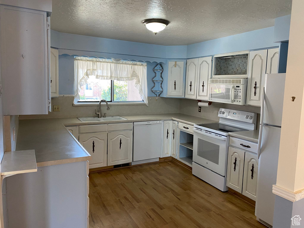Kitchen with white cabinets, a sink, white appliances, a textured ceiling, and wood finished floors