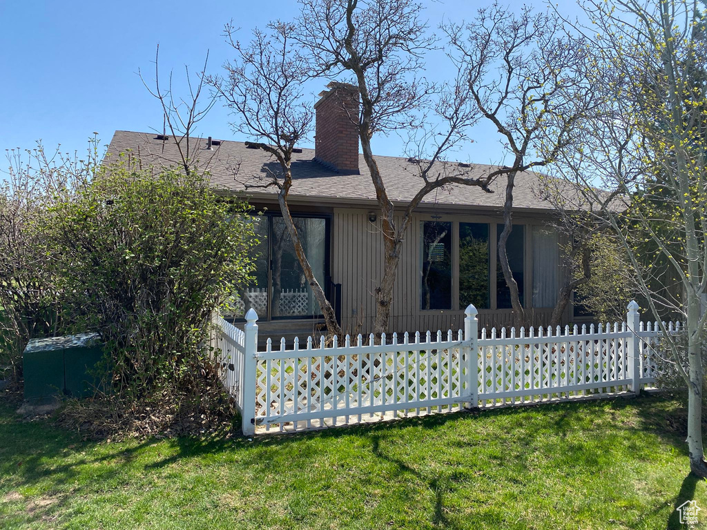 Rear view of property featuring a chimney, a lawn, and a fenced front yard