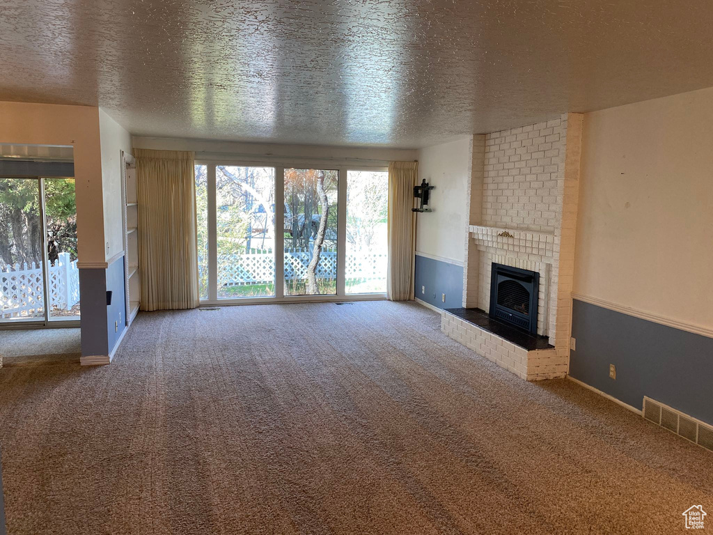 Unfurnished living room featuring visible vents, baseboards, carpet, a textured ceiling, and a fireplace