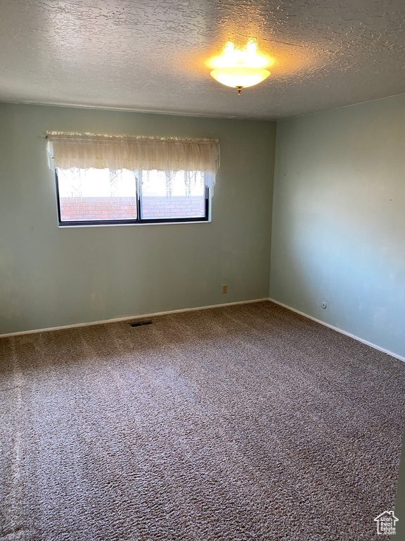 Empty room with a textured ceiling, carpet flooring, baseboards, and visible vents