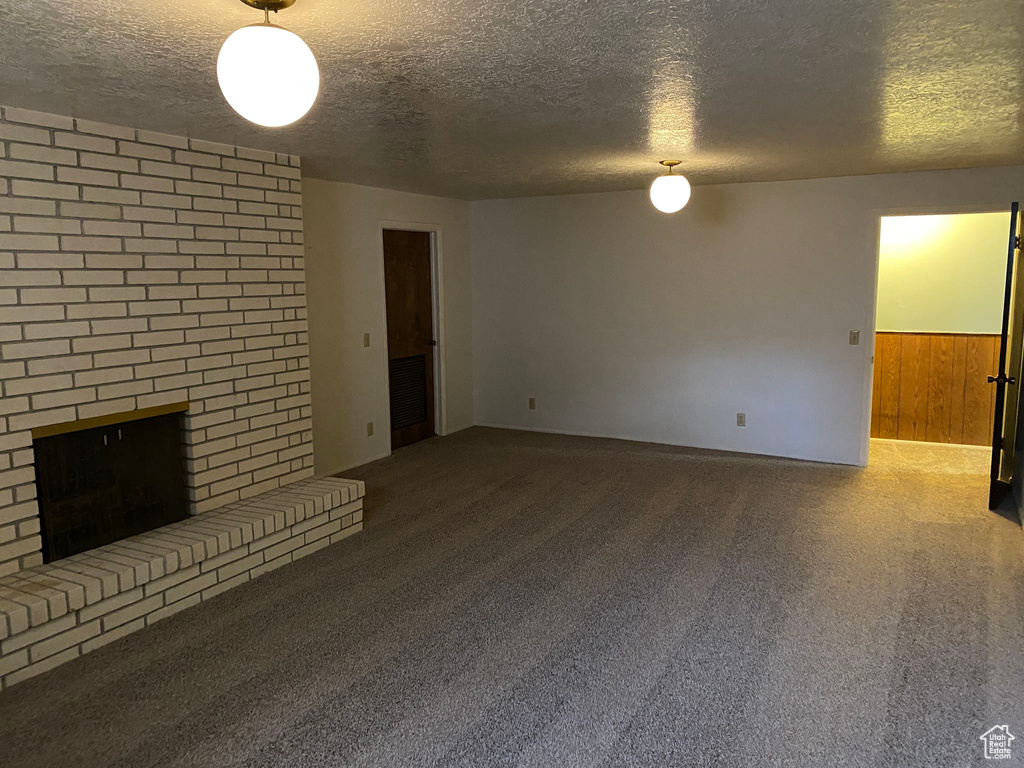 Unfurnished living room featuring carpet floors, wood walls, a fireplace, and a textured ceiling