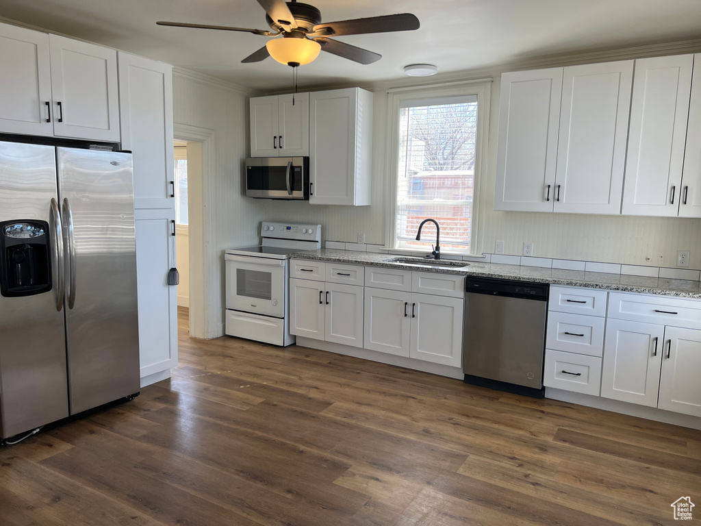 Kitchen with appliances with stainless steel finishes, a sink, dark wood finished floors, and white cabinets