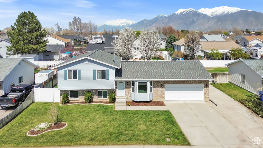 Tri-level home featuring a residential view, fence private yard, a front yard, a mountain view, and driveway