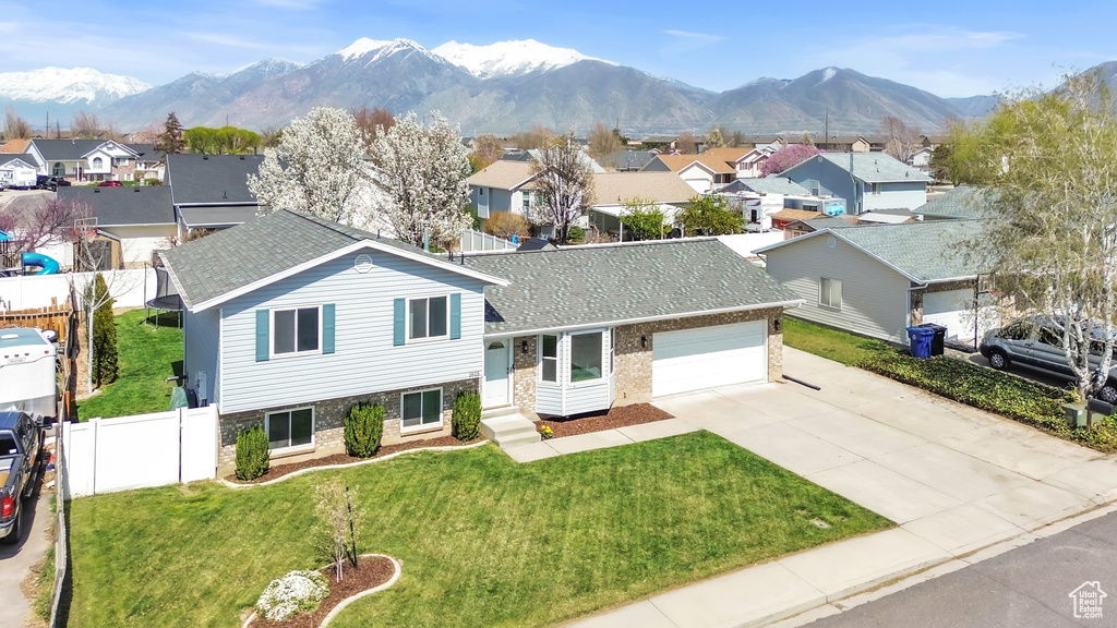 Split level home featuring a residential view, driveway, an attached garage, a front yard, and fence