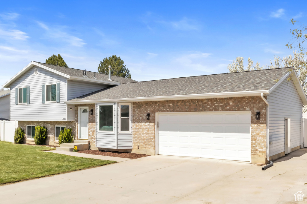 Split level home with a garage, brick siding, driveway, and a front lawn