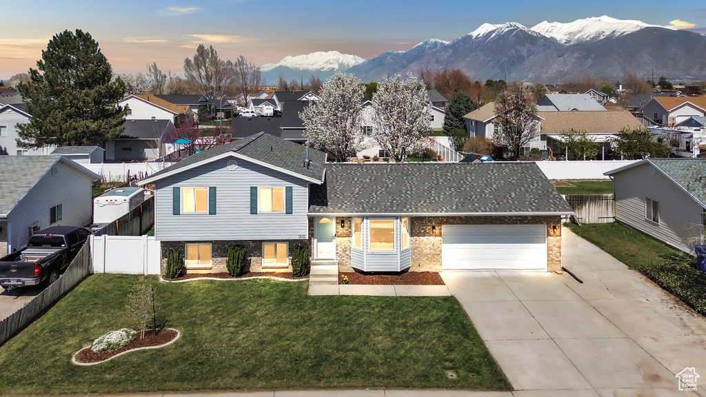 Tri-level home featuring a residential view, a yard, fence, a mountain view, and concrete driveway