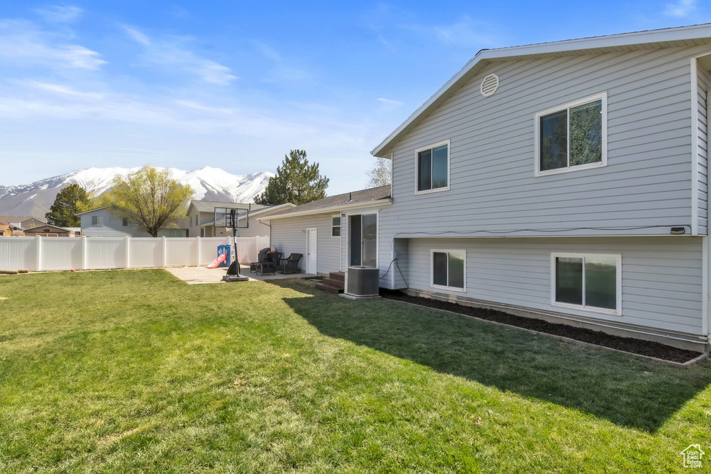 Rear view of house featuring a yard, central air condition unit, fence, and a mountain view