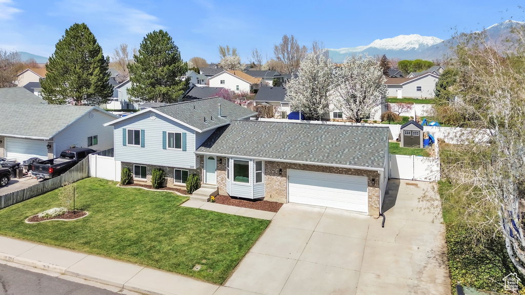 Tri-level home with brick siding, fence, a residential view, and concrete driveway