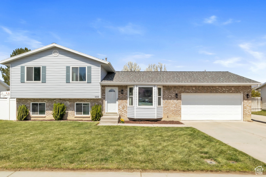 Tri-level home with concrete driveway, a front yard, brick siding, a garage, and a shingled roof