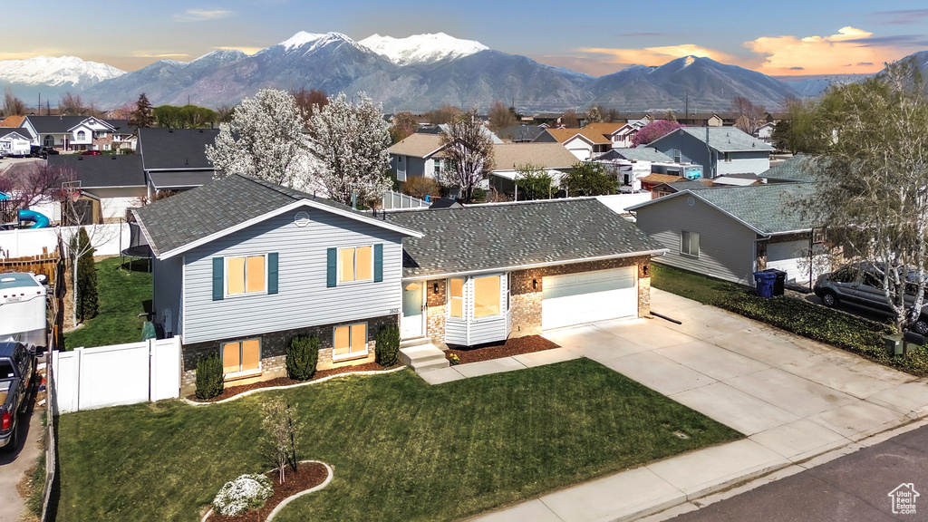 Split level home featuring a residential view, fence, a front lawn, a mountain view, and driveway