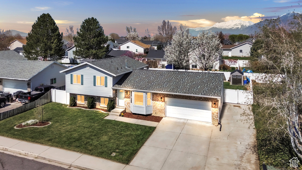 Split level home with driveway, an attached garage, brick siding, a yard, and fence