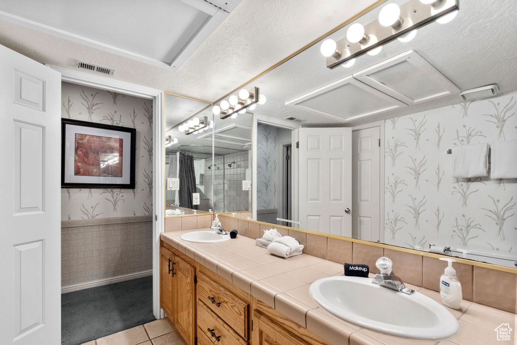 Bathroom with wallpapered walls, visible vents, a sink, and tile patterned floors