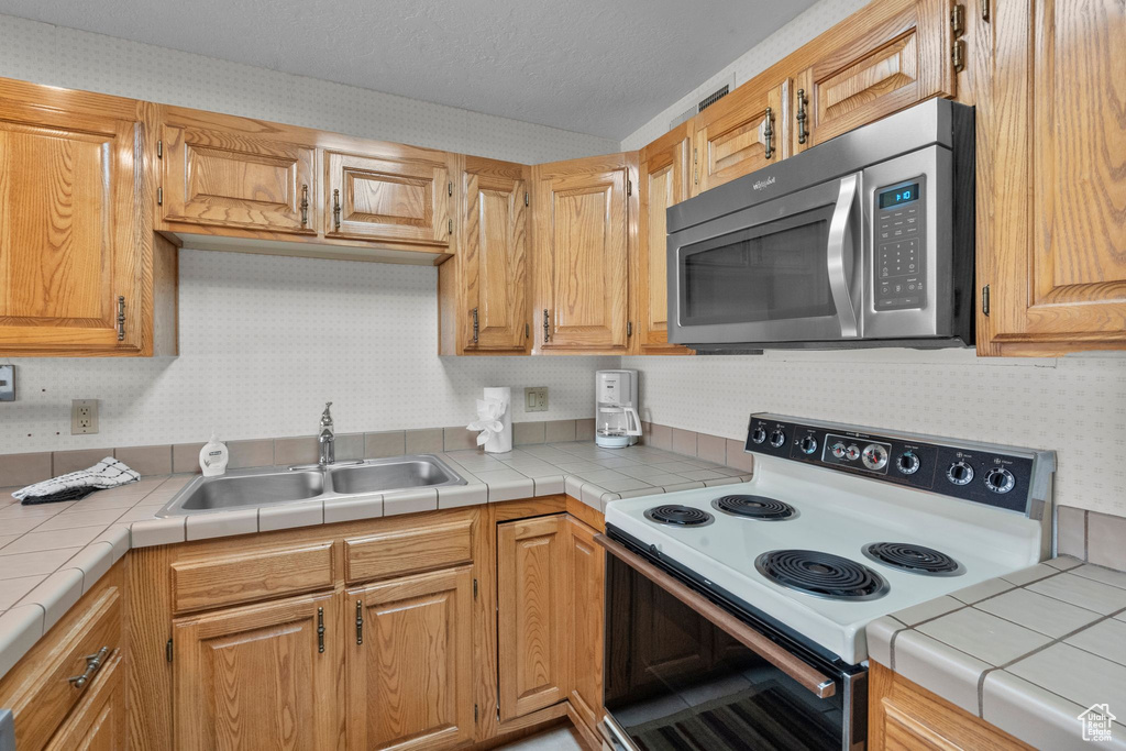 Kitchen with white range with electric cooktop, stainless steel microwave, wallpapered walls, and a sink