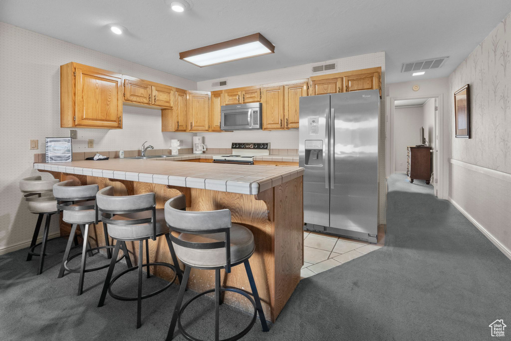 Kitchen with visible vents, a sink, a peninsula, tile counters, and stainless steel appliances