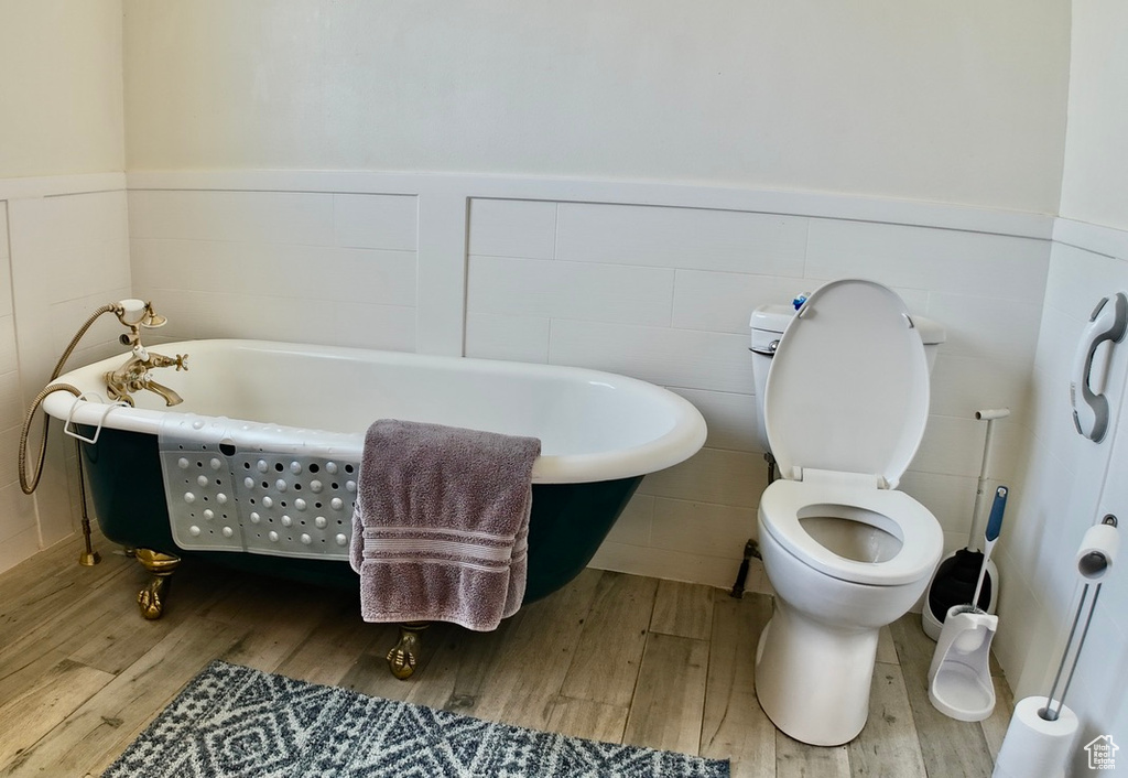 Bathroom featuring toilet, a freestanding tub, wainscoting, and wood finished floors