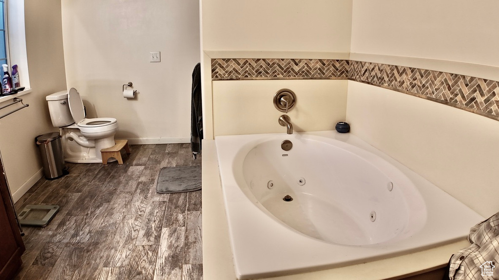 Full bathroom with a whirlpool tub, toilet, wood finished floors, and baseboards