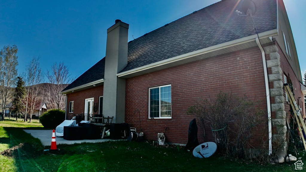 View of side of home with roof with shingles, a chimney, and brick siding