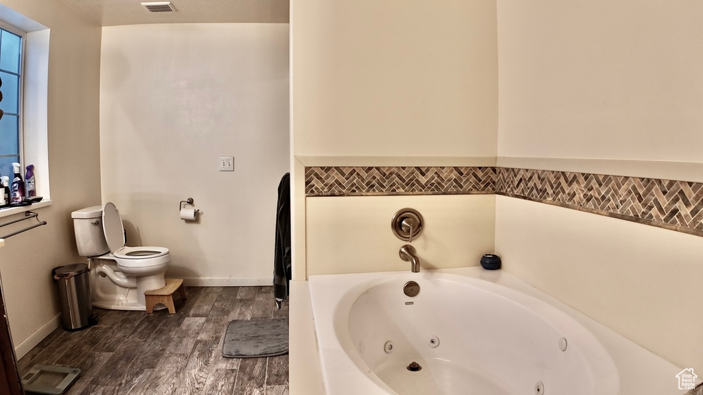 Full bathroom with visible vents, baseboards, toilet, a tub with jets, and wood finished floors