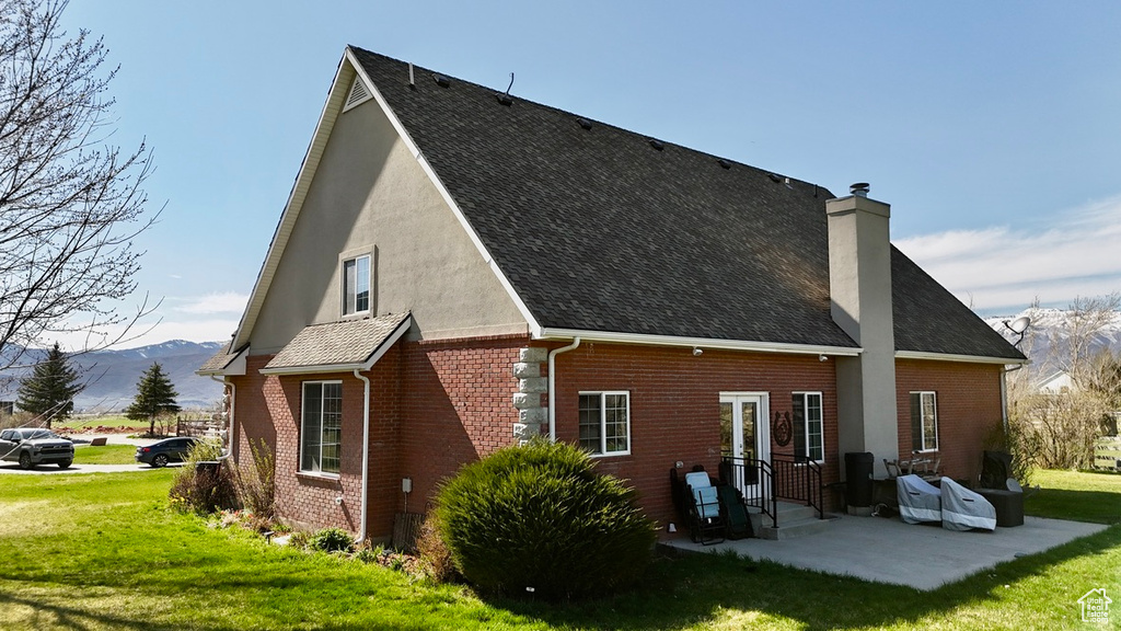 Back of house featuring a lawn, a patio, brick siding, a chimney, and a mountain view