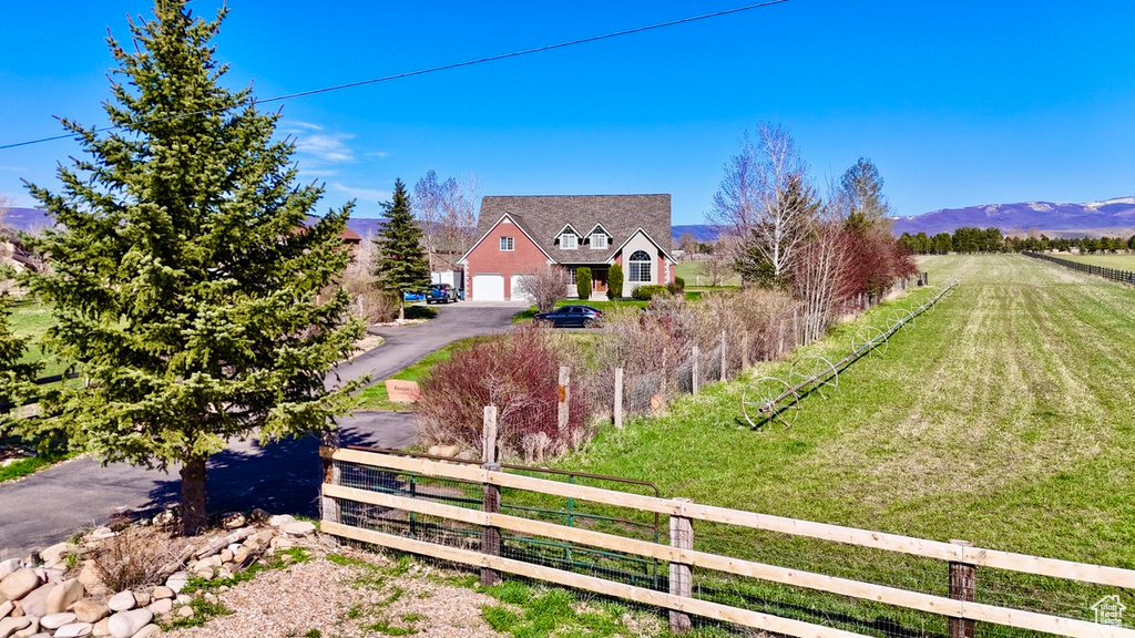 Exterior space featuring a mountain view, a fenced front yard, a rural view, aphalt driveway, and a garage