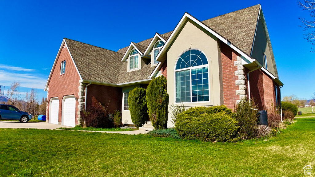 View of front of property with a front yard, an attached garage, brick siding, driveway, and roof with shingles