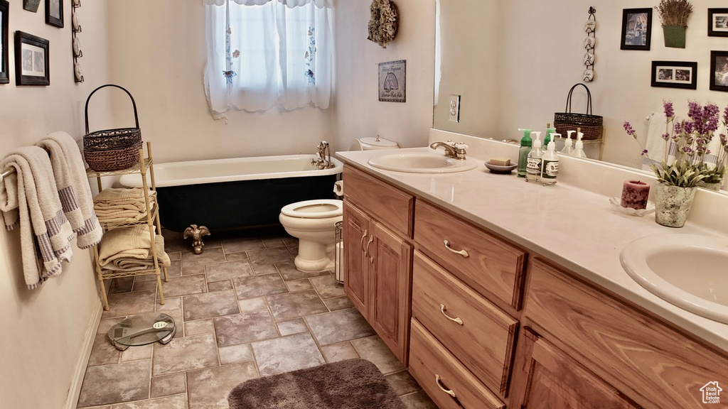 Full bathroom featuring a bath, stone finish flooring, toilet, a sink, and double vanity