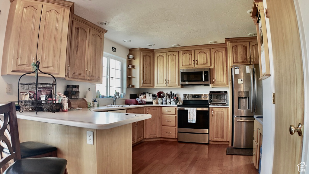 Kitchen featuring open shelves, light countertops, a peninsula, dark wood-style floors, and stainless steel appliances