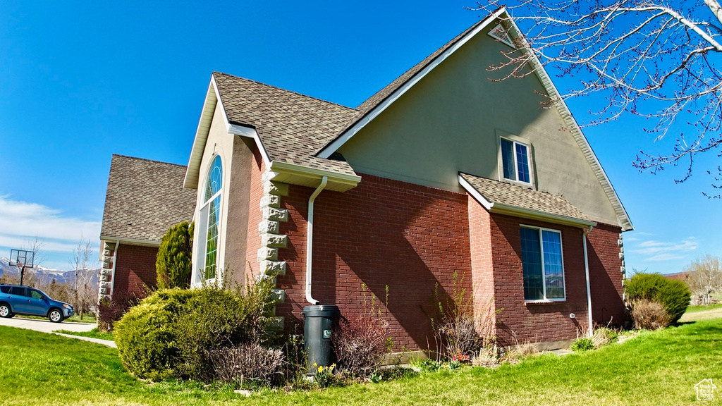 View of side of home featuring roof with shingles, a lawn, stucco siding, and brick siding