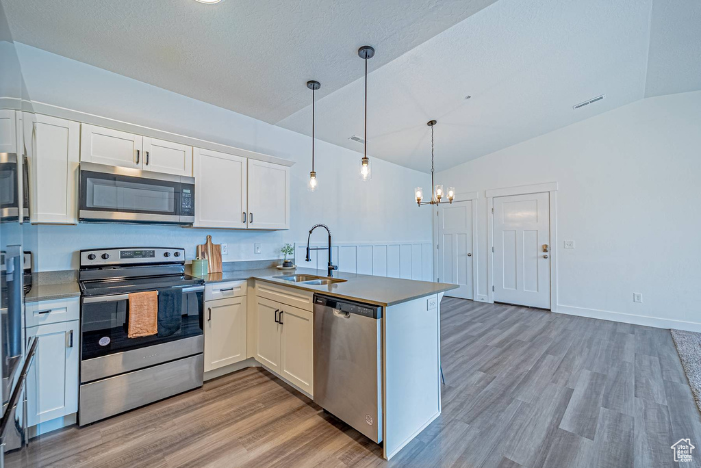Kitchen with a peninsula, vaulted ceiling, a sink, and appliances with stainless steel finishes