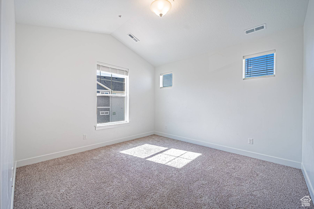 Unfurnished room featuring a healthy amount of sunlight, lofted ceiling, visible vents, and carpet