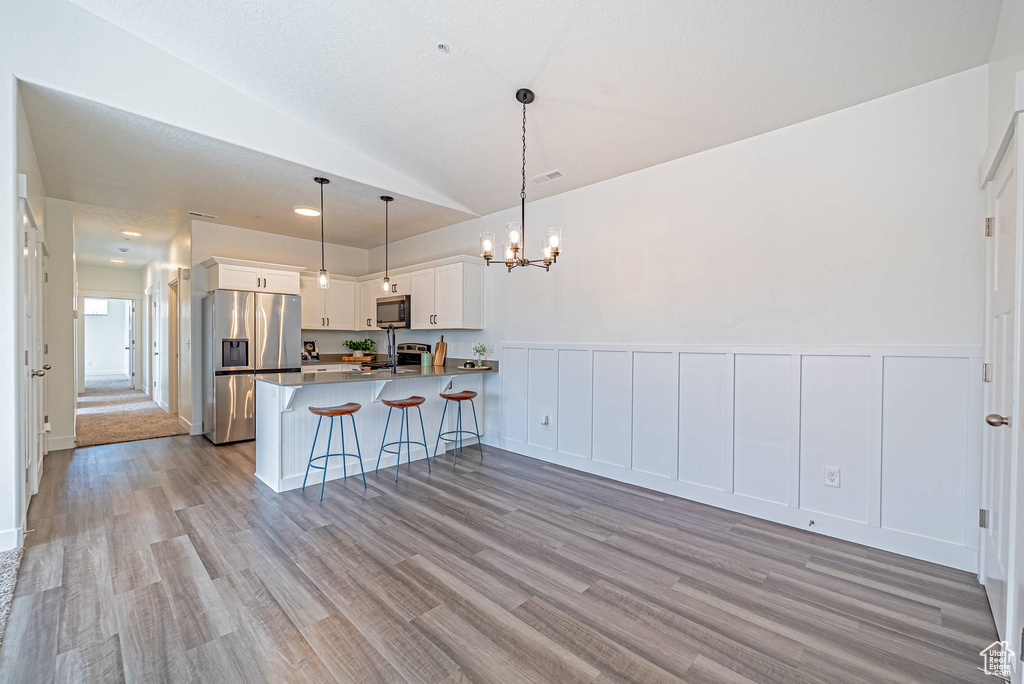 Kitchen with a notable chandelier, light wood-type flooring, a peninsula, white cabinetry, and appliances with stainless steel finishes