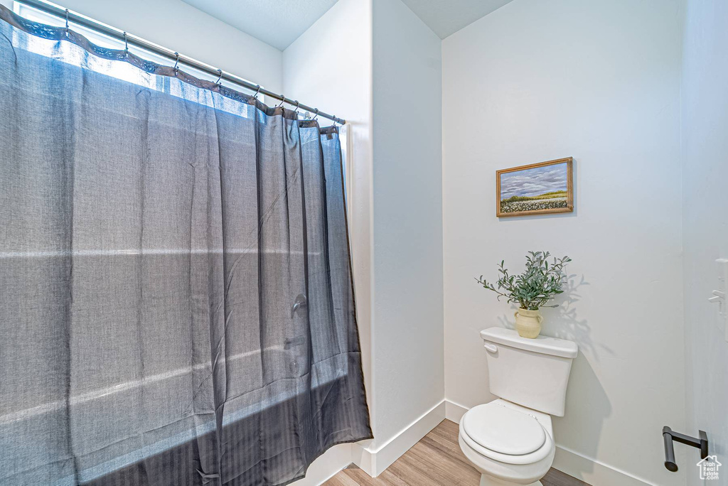 Bathroom featuring toilet, a shower with curtain, wood finished floors, and baseboards