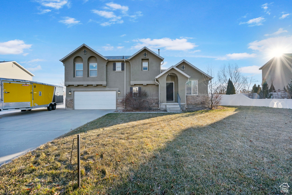 Traditional home with concrete driveway, stucco siding, stone siding, a garage, and fence