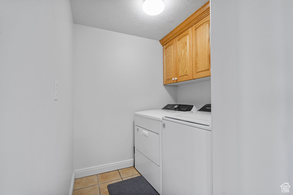 Clothes washing area featuring light tile patterned floors, washer and clothes dryer, baseboards, and cabinet space