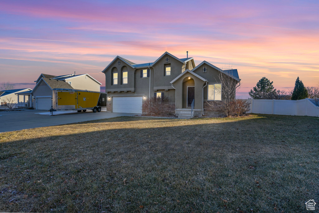 Traditional-style home featuring stucco siding, driveway, an attached garage, fence, and a lawn